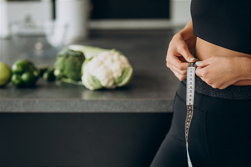 Foto de mulher utilizando uma fita métrica para medir a cintura em uma cozinha