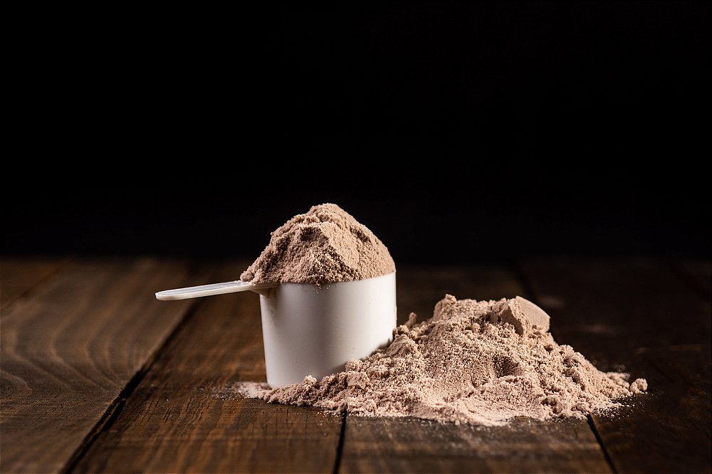 Scoop de whey protein concentrado sabor chocolate belga Soldiers Nutrition sobre uma mesa de madeira