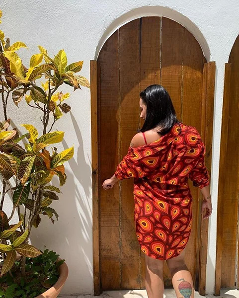 mulher de costas abrindo uma porta de madeira vestindo uma chemise estampada