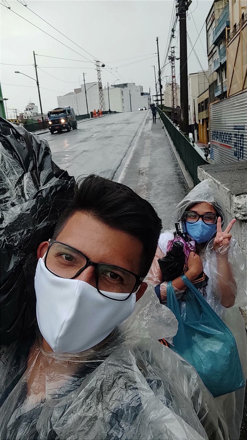 Danielle e Denis de capa de chuva entregando pedidos na rua durante a pandemia