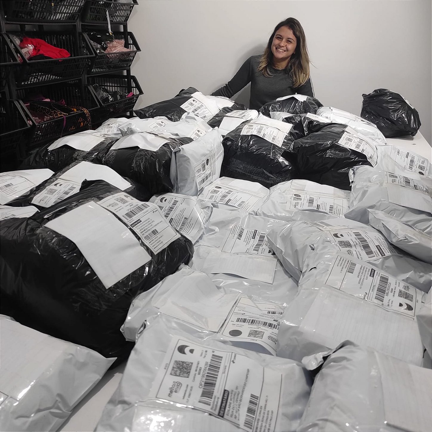 Danielle sorrindo cercada por centenas de pedidos embalados e prontos para envio