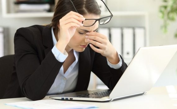 Mulher de óculos com dor de cabeça em frente ao computador devido a alta exposição a tela do computador
