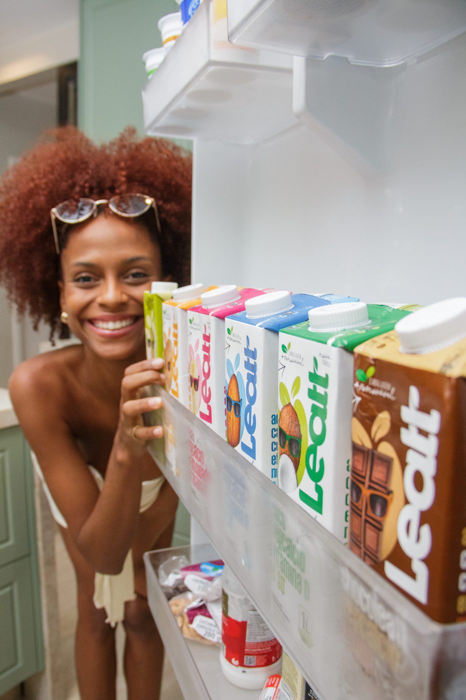 Mulher sorrindo ao lado das embalagens de leite vegetal Leatt na geladeira