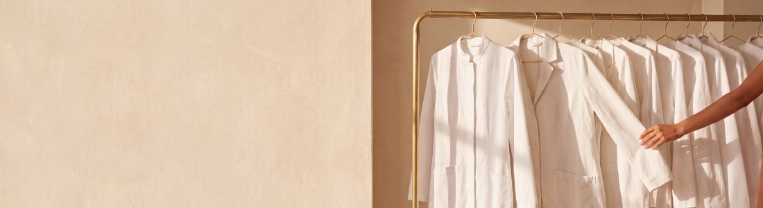 Jalecos brancos de modelos e comprimentos diferentes pendurados em arara