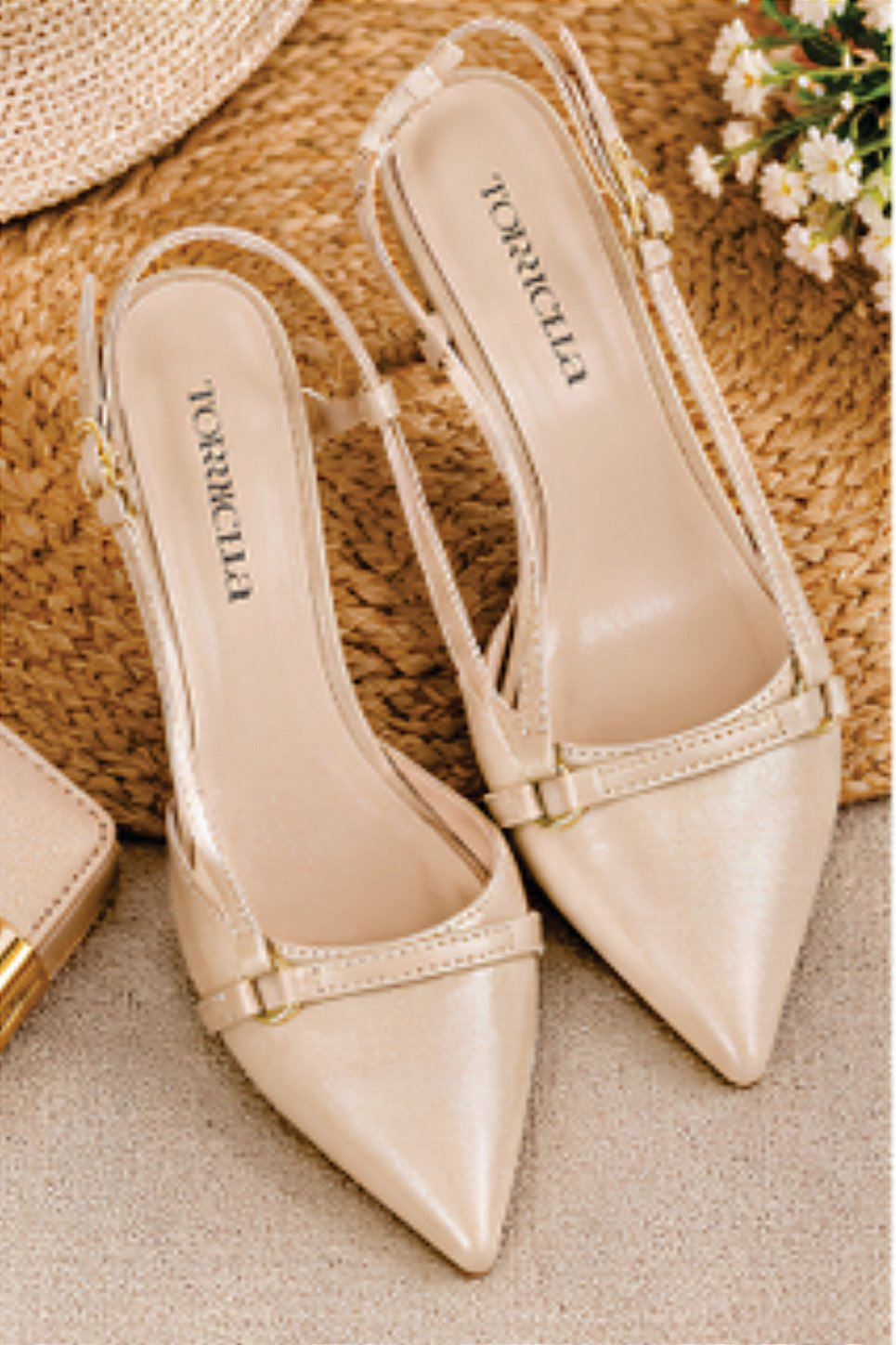 Sapato scarpin feminino modelo slingback de bico fino na cor napa Bege Torricella com fivela dourada, exposto sobre uma mesa de vidro em uma galeria de arte moderna luxuosa.