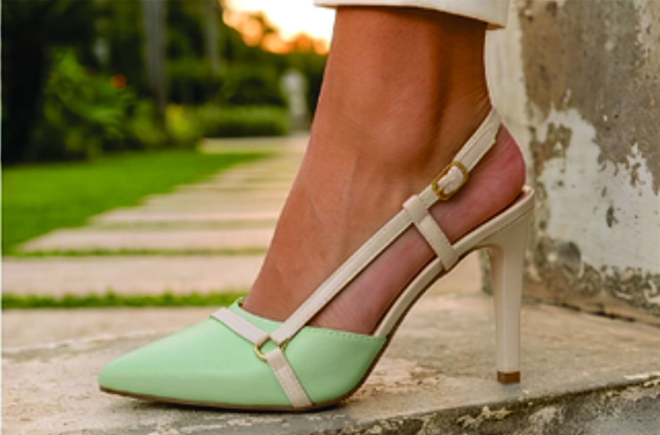 Sapato scarpin feminino modelo slingback de bico fino na cor napa Verde Torricella com fivela dourada, exposto sobre uma mesa de vidro em uma galeria de arte moderna luxuosa.08