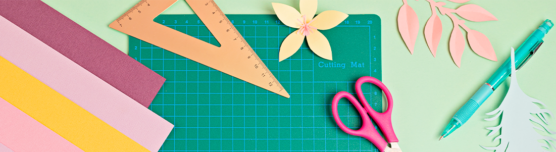 Foto de uma base de corte, papéis cortados e materiais para realizar a produção