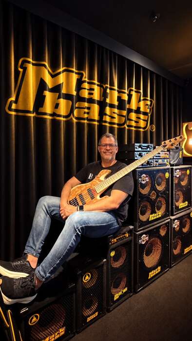 Fabio Lessa sentado em stacks de amplificadores Mark Bass, segurando um contrabaixo