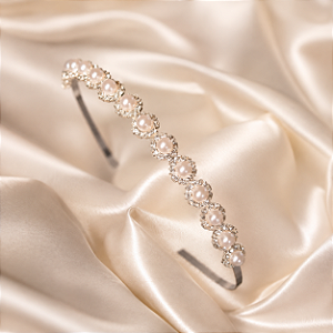 Tiara Feminina Prateada com Pérolas e CristaiTiara feminina em metal com banho prateado, delicadamente decorada com pérolas e cristais brancos, que proporcionam brilho e sofisticação ao visual. O design clássico e elegante valoriza penteados e produções p