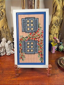 Quadro em tapeçaria com janelas e flores.
