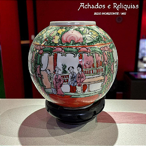 Vaso em porcelana chinesa policromada, representando cena de figuras em um ambiente tradicional, ornamentado com motivos florais e frutíferos. Apoiado sobre suporte em madeira entalhada.