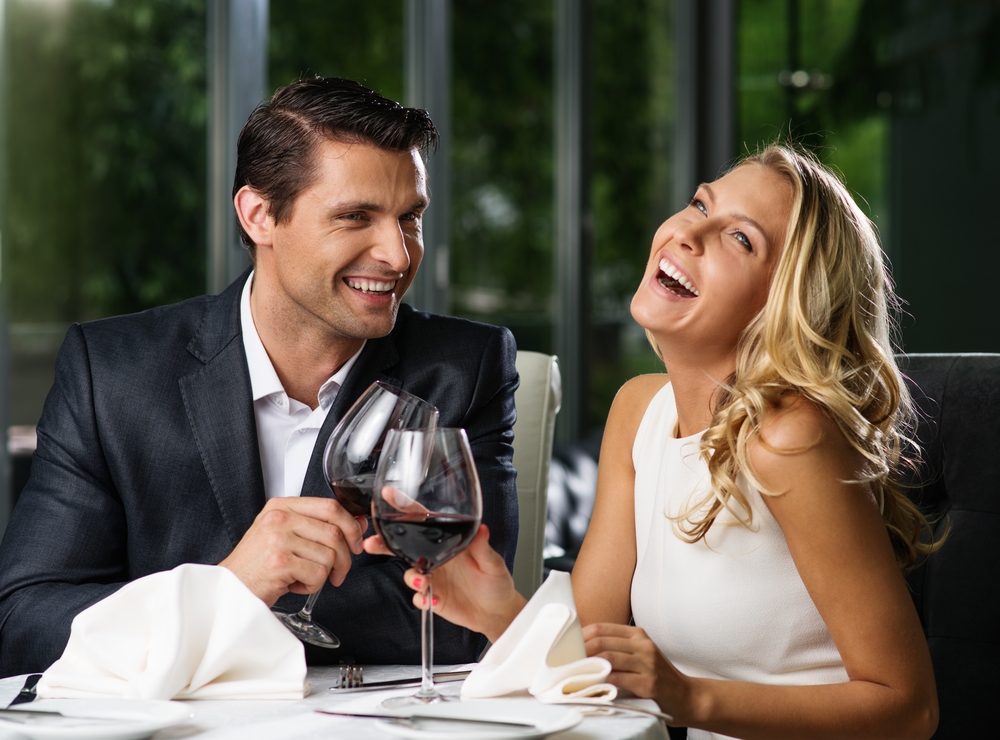 homem de terno e mulher de vestido branco sorrindo e tomando vinho