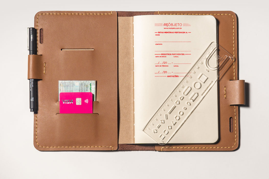 A capa para cadernos A5 possui slots para cartões e documentos, bolso para Kindle ou iPad mini e vem acompanhada de uma régua exclusiva.