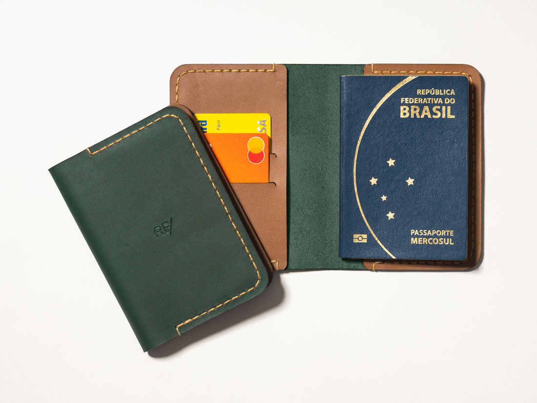 Capa para passaporte feita em couro verde e caramelo, com slots para cartões de crédito e débito, bolsos para dinheiro em espécie e documentos.