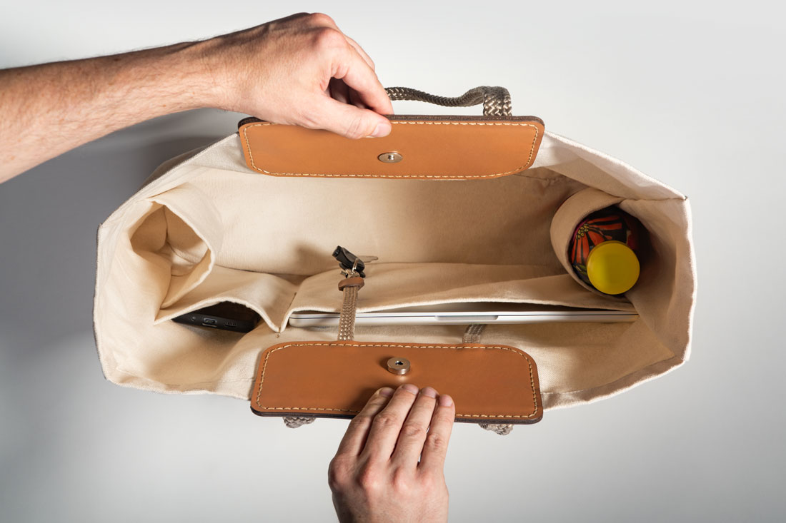 O espaço interno da Tote Bag Duna é generoso e possui divisórias otimizadas para os itens do dia a dia. Na imagem, um Macbook Air de 13”, um smartphone iPhone 17 e uma garrafa d'água, além de chaves presas no mosquetão.