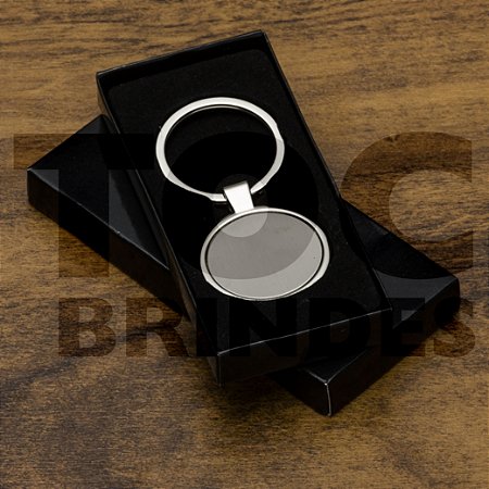 Chaveiro em aço brilhante, redondo, com chapa central fosca, argola alto brilho e caixinha em papel com berço em plástico preto aveludado