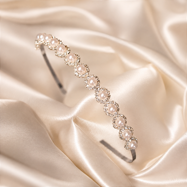 Tiara Feminina Prateada com Pérolas e CristaiTiara feminina em metal com banho prateado, delicadamente decorada com pérolas e cristais brancos, que proporcionam brilho e sofisticação ao visual. O design clássico e elegante valoriza penteados e produções p