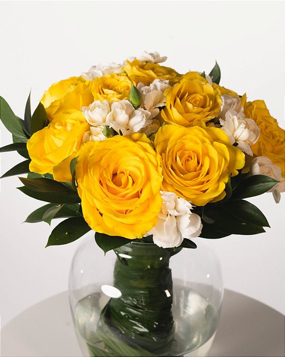 BUQUÊ ELEGANCE-ROSAS AMARELAS E CRAVINAS BRANCAS NO VASO DE VIDRO COM FOLHAGENS DE CANOA