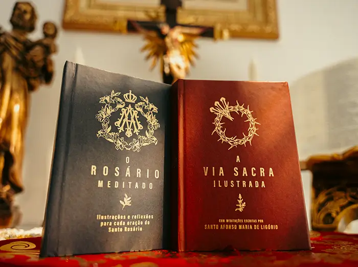 Combo Meditações ilustradas com Rosário Meditado e Via Sacra ilustrada lado a lado sobre uma mesa
