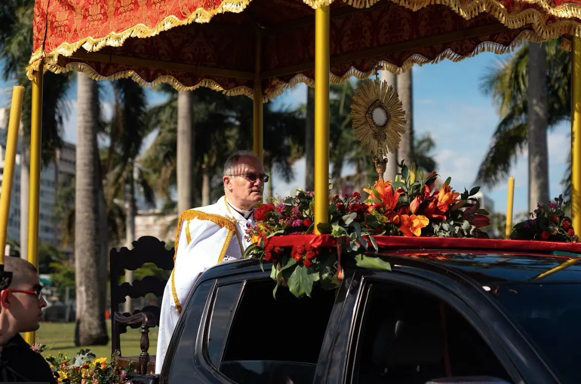 Dom Bernard Fellay na procissão solene de Cristo Rei no Rio de Janeiro, centenário da Quas Primas. Bispo Dom Bernard Fellay, em paramentos pontificais brancos e dourados, em uma procissão sob um dossel. O Santíssimo Sacramento está exposto sobre um carro ricamente florido, celebrando o centenário da festa de Cristo Rei instituída por Pio XI, em 26 de outubro de 2025.