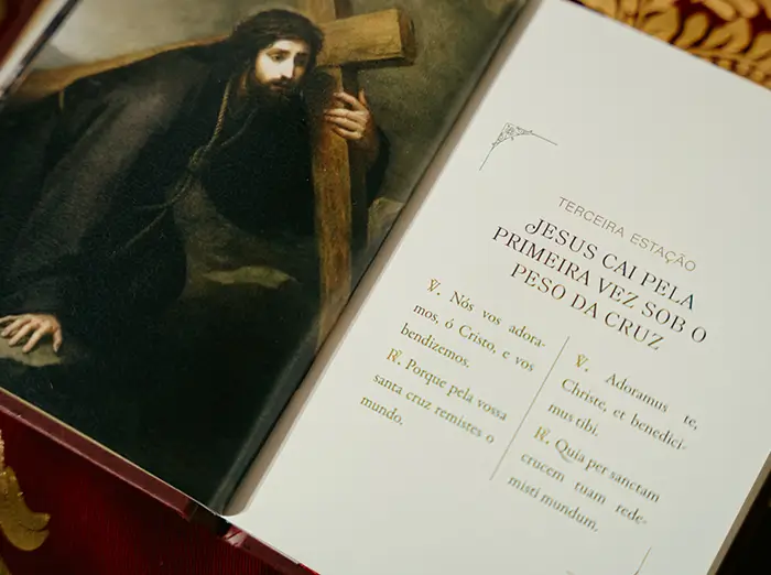 Livro A Via Sacra Ilustrada aberto em uma página que tem a ilustração de Jesus Carregando a Cruz