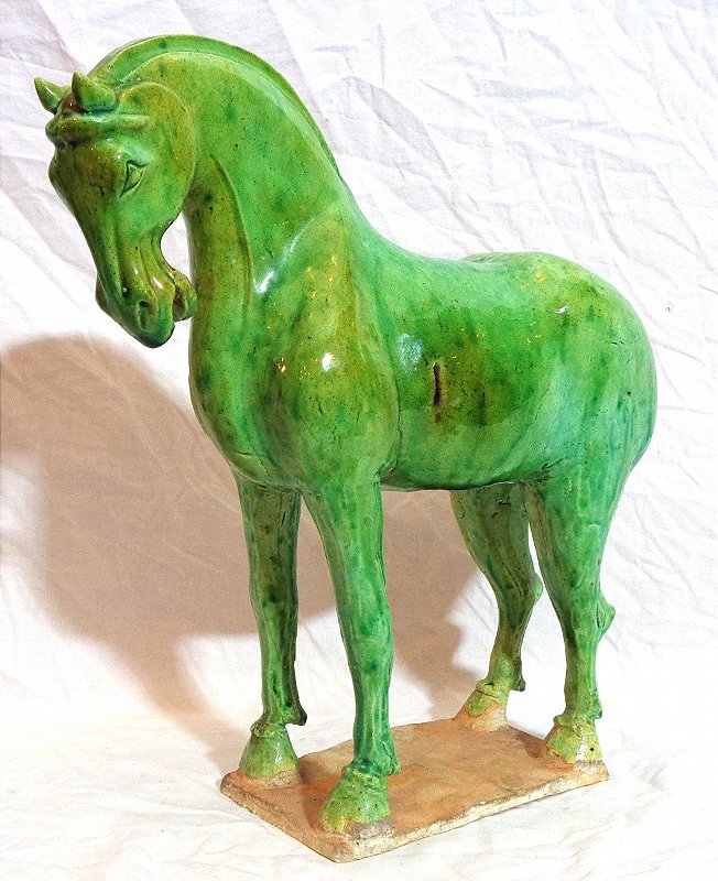Estatueta chinesa modelada em cavalo, ao gosto do período tang. Coberta por esmalte tonalidade verde. Séc. XX. Med. Alt. 27.5 cm. x Compr. 27 cm.