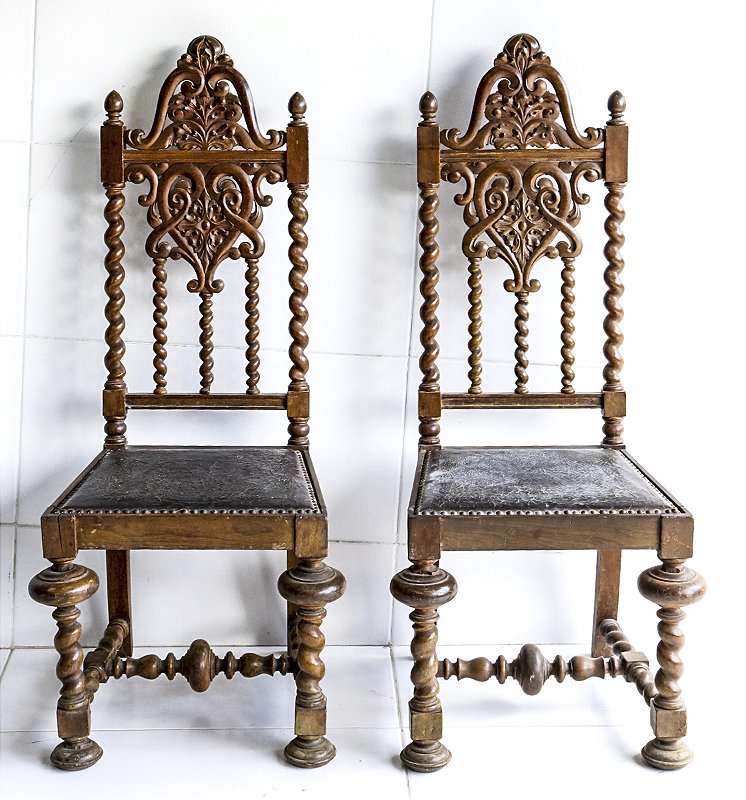 Par de cadeira em madeira nobre, estilo Manuelino, assento em couro lavrado e encosto entalhado. Med. 120x53x45 cm