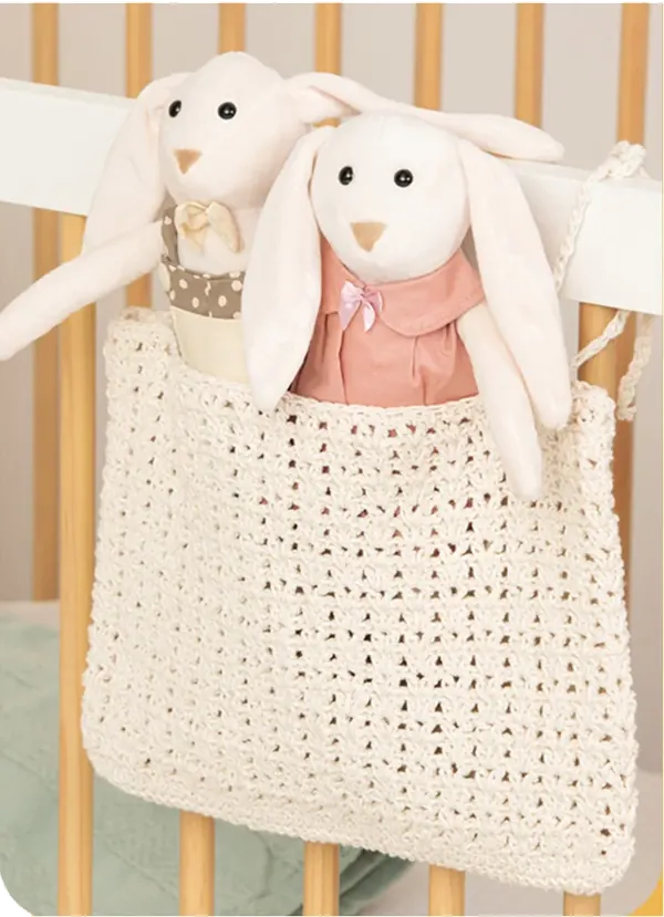 Coelhinhos de pelúcia na bolsa de crochê pendurada no berço